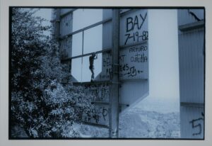 photograph of person walking on I-Beams on the back of a billboard covered in graffiti